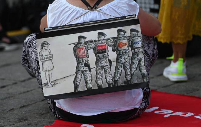 Une femme porte une pancarte où des soldats, représentant divers médias allemands, visent une jeune femme « Vérité » lors d’une manifestation contre les restrictions liées à la pandémie de coronavirus à Dortmund, le 9 août 2020.