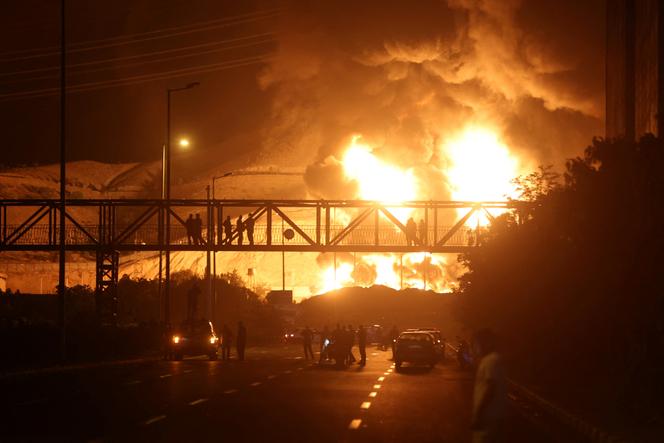Des gens regardent depuis un pont les flammes d’une attaque israélienne s’élever du dépôt pétrolier de Shahran, après les frappes israéliennes contre l’Iran, à Téhéran, le 15 juin 2025.