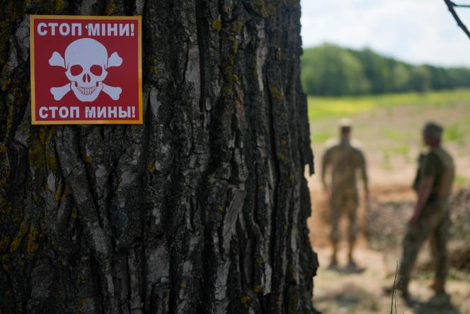 Un avis d’avertissement est fixé à un arbre alors qu’une équipe spécialisée ukrainienne recherche des mines dans un champ à la périphérie de Kiev, le jeudi 9 juin 2022.