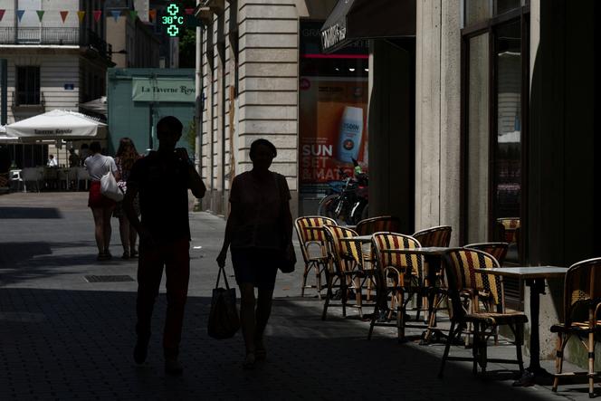 Des passants dans une rue où le thermomètre d’une pharmacie affiche une température de 38 °C, à Nantes, le 20 juin 2025.