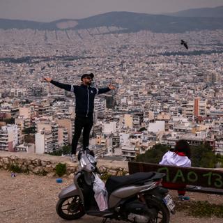 A man poses atop a hill overlooking the city of Athens on April 15, 2025. On the hills of Kypseli, one of Athens' most densely populated neighborhoods, residents stroll through a small park recently created to bring a breath of fresh air when the Greek capital is sweltering, an initiative that residents and experts say is long overdue. Most of Athens' buildings and streets were built with materials more than 40 years old, which absorb heat in the summer. (Photo by Aris Messinis / AFP)