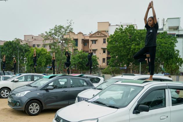 Young members of a yoga institute practice yoga on parked cars in Ahmedabad, India, on June 21, 2025.
