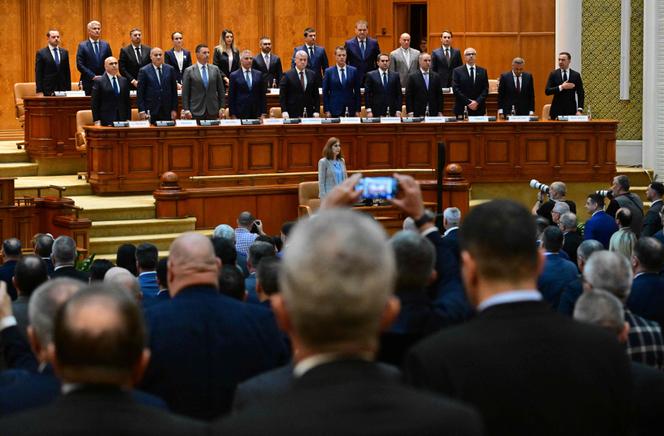 Le nouveau premier ministre roumain, Ilie Bolojan (première rangée, à gauche), et les membres de son cabinet se lèvent pendant l’hymne national au Palais du Parlement, à Bucarest, le 23 juin 2025.