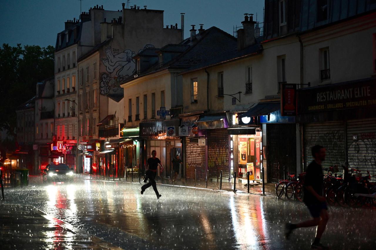 Des personnes courent se mettre à l’abri dans une rue du 20ᵉ arrondissement, à Paris, le 25 juin 2025. 