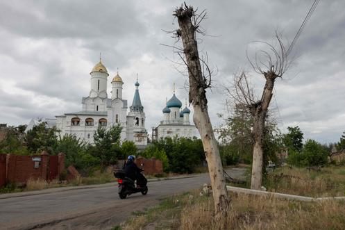 Une femme passe en scooter devant une église endommagée, dans la ville de Sviatohirsk, dans l’oblast de Donetsk, le 26 juin 2025.