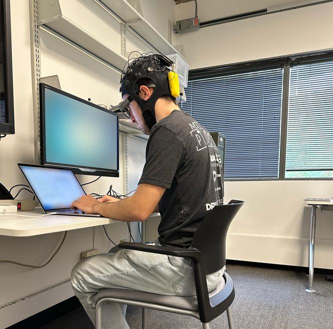 Un des volontaires de l’expérience, à l’œuvre sur rédaction, portant des lunettes AttentivU et un casque avec 32 canaux, outils mesurant l’activité cérébrale (encéphalogramme) et les flux d’informations circulant dans différentes zones du cerveau (dDTF). En janvier 2024, au MIT Media Lab, à Cambridge (Massachusetts).