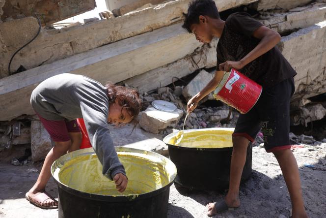 Des enfants raclent le fond de marmites à un point de distribution de nourriture à Gaza, le 27 juin 2025.