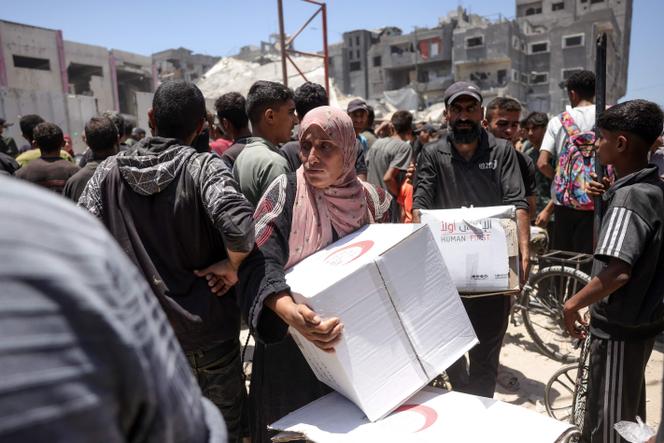 Des palestiniens transportent des cartons d’aide distribués par le Croissant Rouge, à Gaza, le 26 juin 2025.