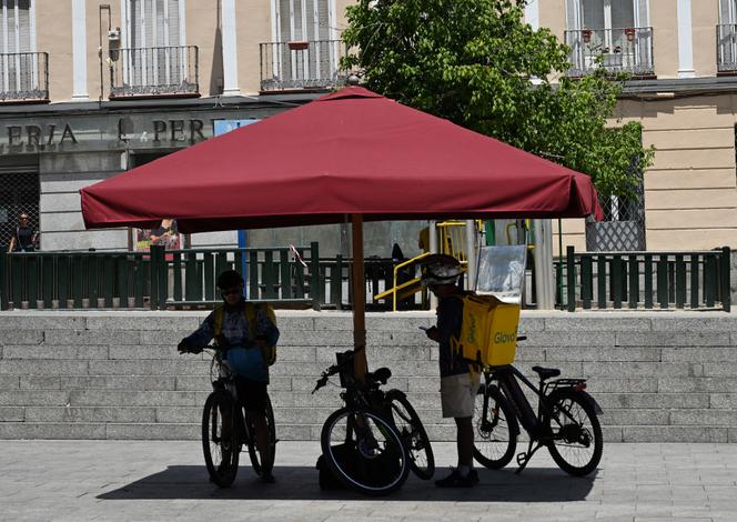 Des livreurs se cachent du soleil sous un parasol à Madrid, le 18 juin 2025, alors qu’une vague de chaleur frappe l’Espagne.