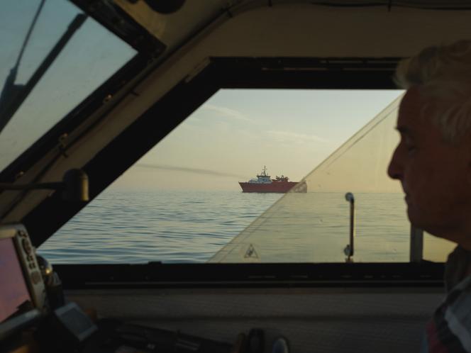 Le « Minck », un bateau affrété par l’Etat pour les opérations de sauvetage dans la Manche, vu de la fenêtre du bateau d’un pêcheur, au large de Dunkerque (Nord), le 1ᵉʳ juillet 2025.