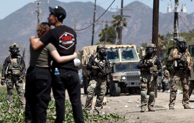 Des personnes s’étreignent près d’agents fédéraux bloquant une route lors d’un raid de l’ICE contre l’immigration dans une ferme de cannabis située à proximité, le 10 juillet 2025, près de Camarillo, en Californie.