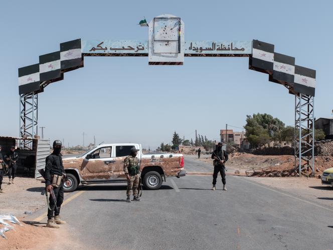 Des membres des forces de sécurité intérieure syriennes (ministère de l’intérieur) sur un check-point établi dans le village d’As Sawara Al Kubra, dans le gouvernorat de Souweïda dans le sud de la Syrie, le 14 juillet 2025. Sur la pancarte au-dessus d’eux, on peut lire « le gouvernorat de Souweïda vous souhaite la bienvenue ».