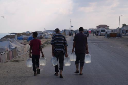Des Palestiniens transportent des bouteilles en plastique contenant de l’eau après qu’ils l’ont récupérée dans un camp de personnes déplacées à Deir Al-Balah (Gaza), le 19 juillet 2025.