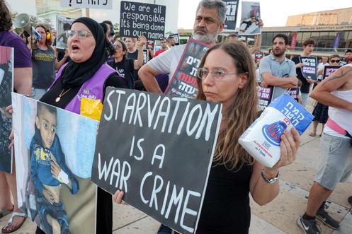 « La famine est un crime de guerre », proclame la pancarte tenue par cette manifestante, qui brandit un sac de farine pour protester contre le quasi blocus alimentaire imposé à Gaza par Israël. A Tel-Aviv, le 22 juillet 2025.