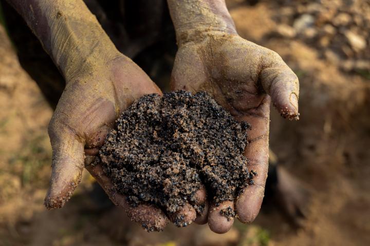 Un creuseur montre une poignée de terre et de roche contenant de la cassitérite et du coltan, à Manono, en RDC, le 20 mai 2025.
