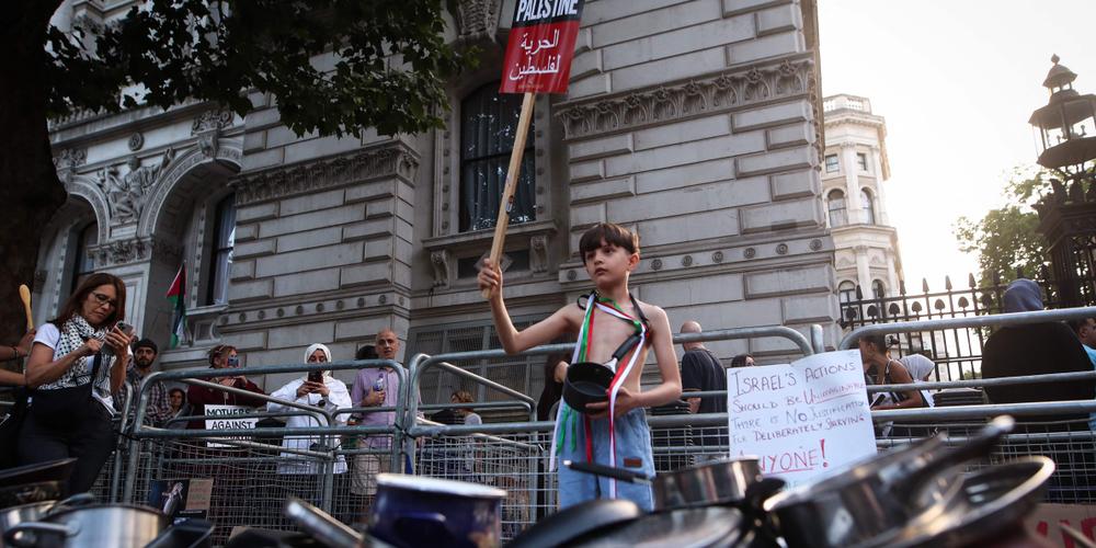 Un enfant tenant une pancarte sur laquelle on peut lire « Free Palestine » se tient derrière des casseroles posées devant les portes de Downing Street, lors d’une manifestation organisée par le groupe Palestine Solidarity Campaign pour protester contre la pénurie de nourriture qui sévit dans la bande de Gaza, à Londres, le 25 juillet 2025. - RHIANNA CHADWICK / AFP