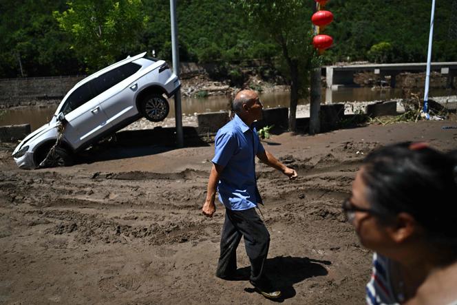 Des passants devant une voiture endommagée par les inondations de ces derniers jours dans le district de Huairou, à la périphérie de Pékin, le 30 juillet 2025.