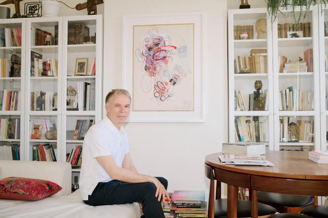 Christian Berst, galeriste spécialisé en art brut, avec une œuvre de Lubos Plny accrochée au mur, dans son appartement, à Paris, le 1ᵉʳ juillet 2025.