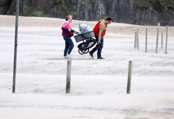People carry their pram across the beach after getting stuck in the sand during Storm Floris on the north coast of Northern Ireland, Portstewart, on August 4 2025. 