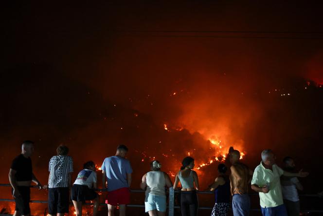 Des personnes ayant évacué leurs maisons, regardent le feu progresser dans le village de Delvina, en Albanie, le 12 août 2025.