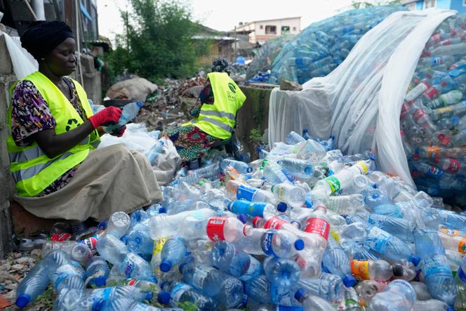 Des ouvriers utilisent des lames de rasoir pour gratter les étiquettes de différentes bouteilles en plastique de boissons gazeuses à la Street Waste Company à Lagos, au Nigeria, le lundi 11 août 2025.