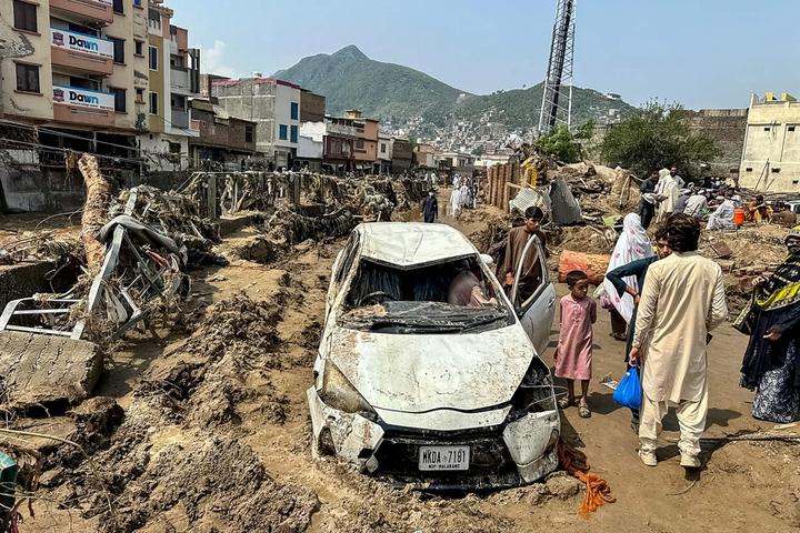 Des personnes se rassemblent près d’un véhicule endommagé et de débris éparpillés après que la route a été emportée par une crue soudaine à Mingora, la principale ville de la vallée de Swat (Pakistan), le 16 août 2025. 