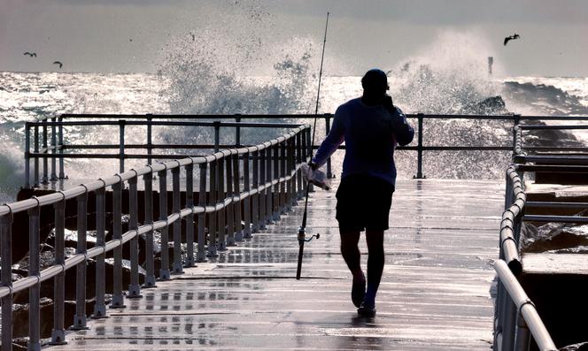 Un pêcheur marche sur une jetée alors que de grosses vagues générées par l’ouragan Erin s’écrasent contre la digue du Lighthouse Point Park, à Ponce Inlet, en Floride, le 20 août 2025.