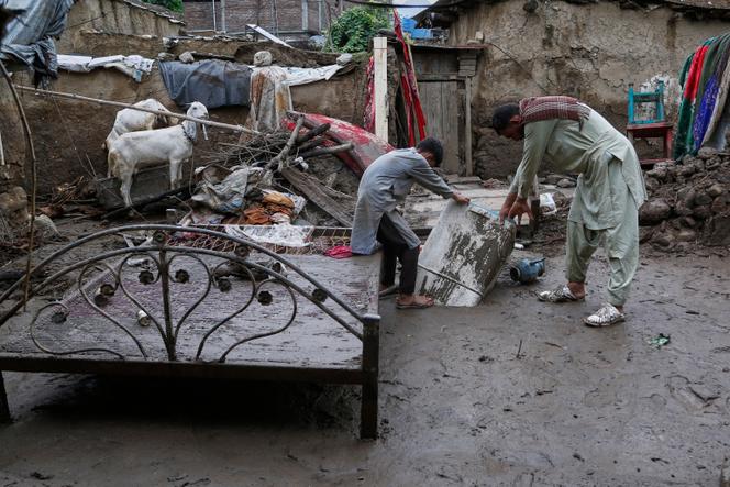 Un père et son fils récupèrent une machine à laver dans la boue de leur maison partiellement détruite par les inondations soudaines qui ont frappé, vendredi, le village de Pir Baba, dans le district de Buner, dans le nord-ouest du Pakistan, dimanche 17 août 2025.