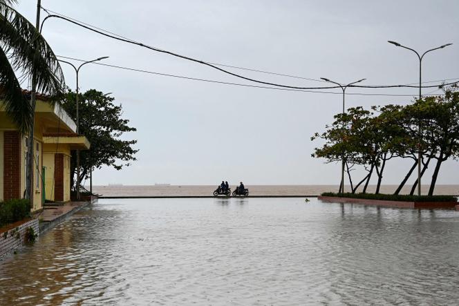 Des personnes se déplacent à moto entre une rue inondée et la plage de Cua Lo après le passage du typhon Kajiki, dans la province de Nghe An, le 26 août 2025.