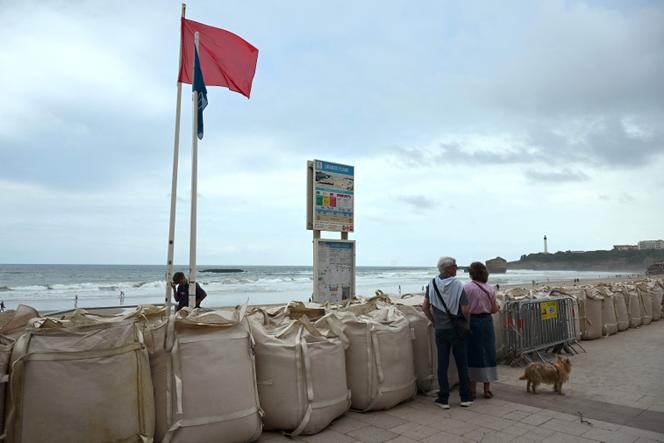 Un drapeau rouge indiquant que la baignade et les sports nautiques sont interdits flotte au-dessus de sacs de sable bloquant l’accès à la Grande Plage de Biarritz (Pyrénées-Atlantiques), en raison d’une houle « cyclonique », le 26 août 2025.