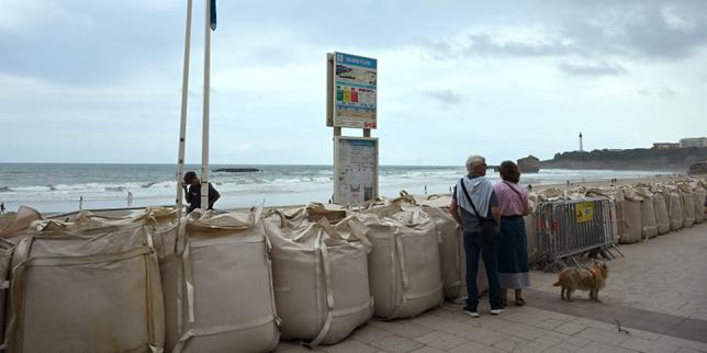 Un drapeau rouge indiquant que la baignade et les sports nautiques sont interdits flotte au-dessus de sacs de sable bloquant l’accès à la Grande Plage de Biarritz (Pyrénées-Atlantiques), en raison d’une houle « cyclonique », le 26 août 2025.