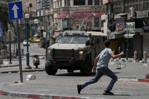 Un Palestinien court devant un véhicule blindé lors d’affrontements avec les forces israéliennes, à la suite d’un raid militaire dans la ville de Naplouse, en Cisjordanie, le 27 août 2025.