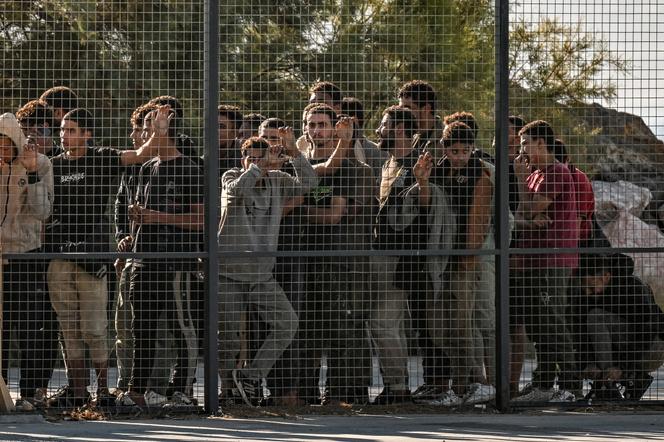 Des migrants sont rassemblés par les gardes-côtes grecs, derrière une clôture, après avoir débarqué d’un cargo dans le port de Lavrio, à Athènes, le 10 juillet 2025.