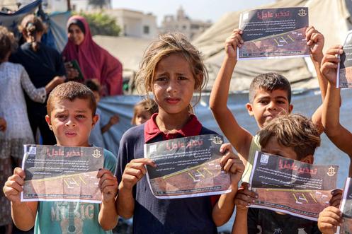 Des enfants palestiniens brandissent les tracts largués par l’armée israélienne appelant à l’évacuation vers la zone humanitaire d’Al-Mawassi, dans la ville de Gaza, le 12 septembre 2025.