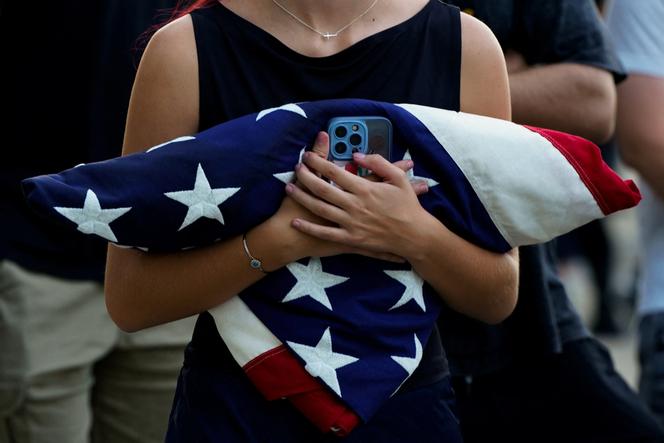 Une femme, un drapeau américain plié dans les bras, attend pour assister à une veillée funèbre après la mort de l’influenceur conservateur Charlie Kirk, à Washington, le 14 septembre 2025.