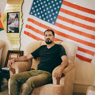 Muhammad Rabee, chez lui, à Turmus Ayya. Derrière lui, entre un drapeau américain et un drapeau palestinien, un portrait de son fils, Omar, 14 ans, abattu le 6 avril 2025 par des soldats israéliens.