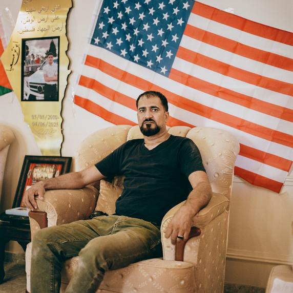 Muhammad Rabee, chez lui, à Turmus Ayya. Derrière lui, entre un drapeau américain et un drapeau palestinien, un portrait de son fils, Omar, 14 ans, abattu le 6 avril 2025 par des soldats israéliens.