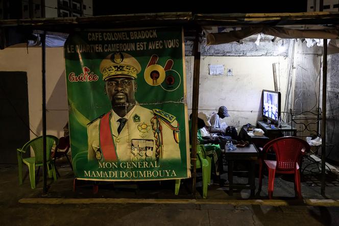 Des habitants regardent la télévision à côté d’une affiche représentant le chef de la junte au pouvoir, Mamadi Doumbouya, avant l’annonce des résultats provisoires du référendum, à Conakry, le 23 septembre 2025.