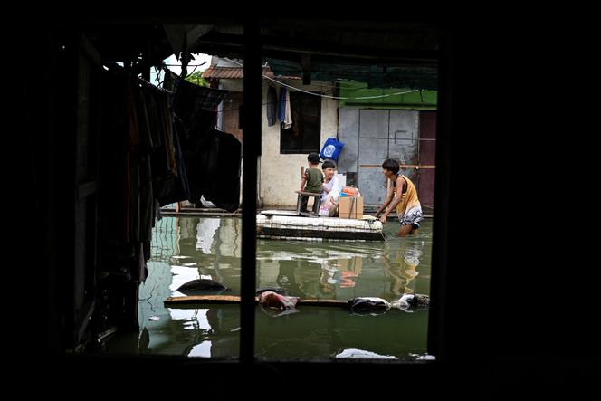Des enfants utilisent un radeau de fortune pour traverser une rue inondée à la suite des pluies, intensifiées par la violente tempête tropicale Bualoi, dans la province de Laguna, aux Philippines, le 26 septembre 2025.  