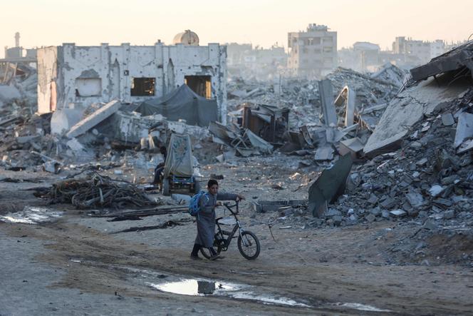 A Palestinian boy pushes his bicycle past the ruins of destroyed buildings in the Sheikh Radwan neighborhood of Gaza City on October 22, 2025.
