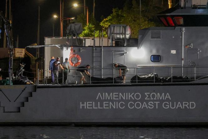 Des hommes transfèrent des sacs mortuaires contenant les corps de migrants décédés après le naufrage de leur bateau en pleine mer au large de la Grèce, à bord d’un navire des garde-côtes helléniques dans le port de Kalamata, en Grèce, le 14 juin 2023. 