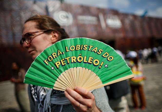 Une manifestante tient un éventail sur lequel il est écrit « lobbyistes pétroliers dehors » lors de la COP30 à Belem (Brésil), le 11 novembre 2025.