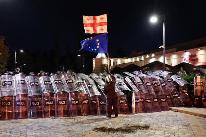 Un manifestant avec les drapeaux géorgien et européen devant les forces antiémeute, lors d’un rassemblement de l’opposition le jour des élections locales dans le centre de Tbilissi, le 4 octobre 2025. 