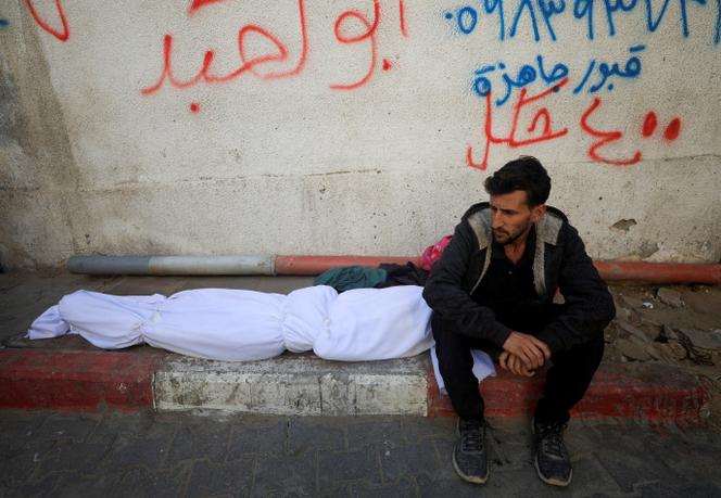 Un homme assis à côté du corps d’un Palestinien qui, selon les médecins, a été tué lors de frappes israéliennes nocturnes, à l’hôpital Al-Shifa de Gaza, le 20 novembre 2025.
