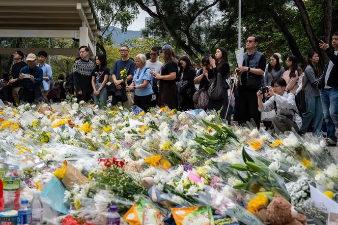 Des personnes prient, dimanche 30 novembre 2025 à Hongkong, devant des fleurs déposées en hommage aux victimes de l’incendie qui a ravagé un complexe résidentiel de Hongkong quatre jours auparavant.
