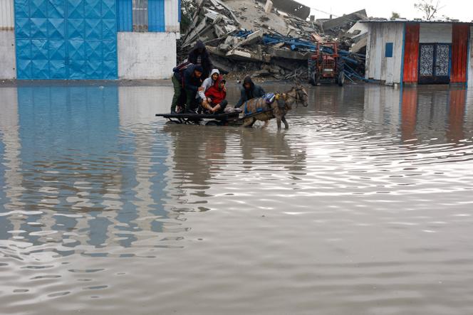 Des Palestiniens déplacés voyagent à bord d’une charrette tirée par un âne dans une rue inondée par la pluie dans la ville de Gaza, le 12 décembre 2025.