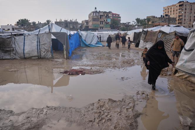 Des Palestiniens traversent une zone inondée dans un campement provisoire après de fortes pluies à Deir Al-Balah, dans le centre de la bande de Gaza, le 12 décembre 2025. 