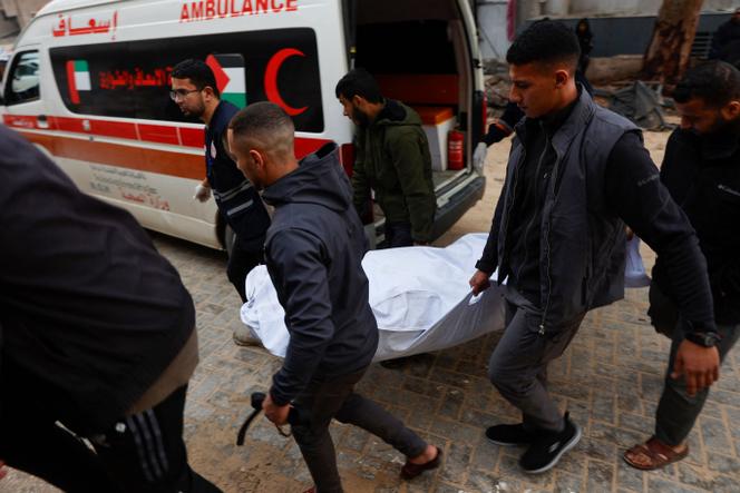 Des Palestiniens et des secouristes transportent le corps d’une victime dans un sac mortuaire à l’hôpital Al-Shifa, visé par une frappe israélienne sur une voiture à Gaza, le 13 décembre 2025. 
