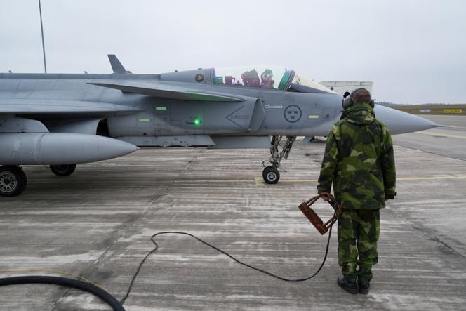 Un membre du personnel au sol de l’escadre de Blekinge de l’armée de l’air suédoise se tient à côté d’un avion de chasse JAS 39 Gripen avant l’un des vols annuels de démonstration aérienne « Sapin de Noël » à Kallinge, en Suède, le 16 décembre 2025.