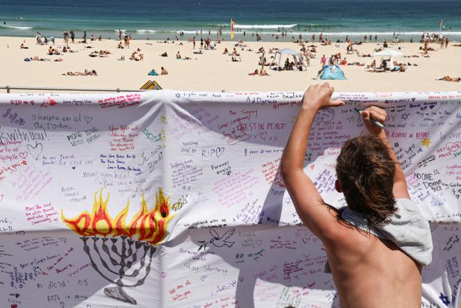 Une personne endeuillée écrit un message sur un morceau de tissu le long de la promenade de Bondi Beach à Sydney, le 18 décembre 2025, en hommage aux victimes de l’attentat qui s’est produit à cet endroit le 14 décembre.